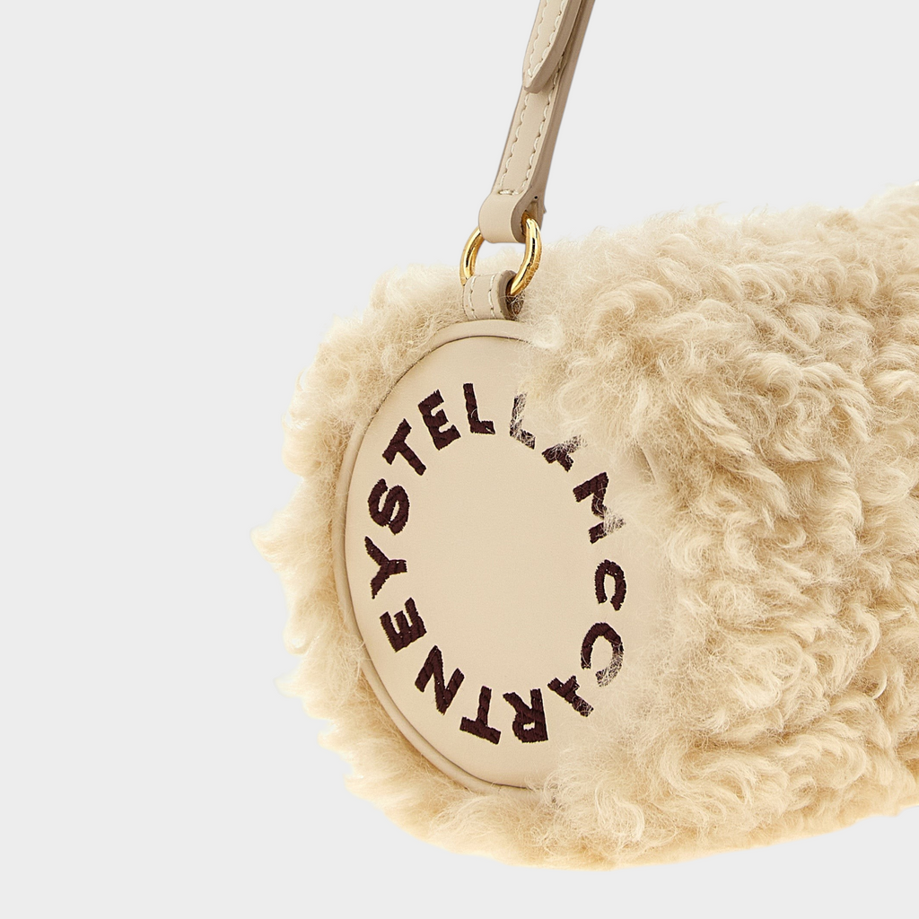 Esmire & Co beige cylindrical clutch with sheepskin-effect texture, gold hardware, and Stella McCartney logo detail.